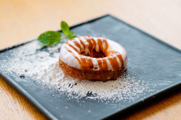 Karamell-Donut mit Zuckerstreuseln auf einem schwarzen quadratischen Teller Leckeres Dessert mit einer Scheibe Minze