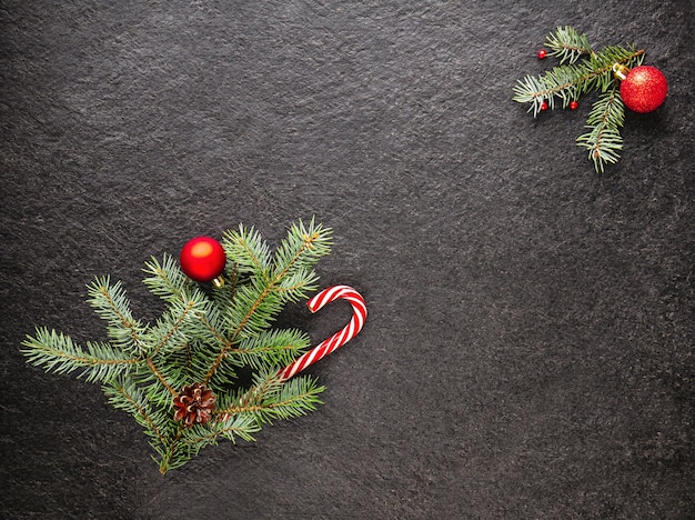 Karamellstock mit Ästen stößt Perlen und Weihnachtsbaumspielzeug auf dunklem Hintergrund