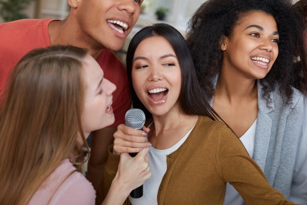 Karaoke-Partygruppe junger und glücklicher multikultureller Freunde in Freizeitkleidung, die mit Mikrofon singen