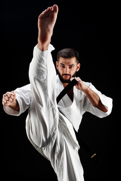 Karate-Mann im Kimono schlägt mit dem Fuß auf schwarzem Hintergrund