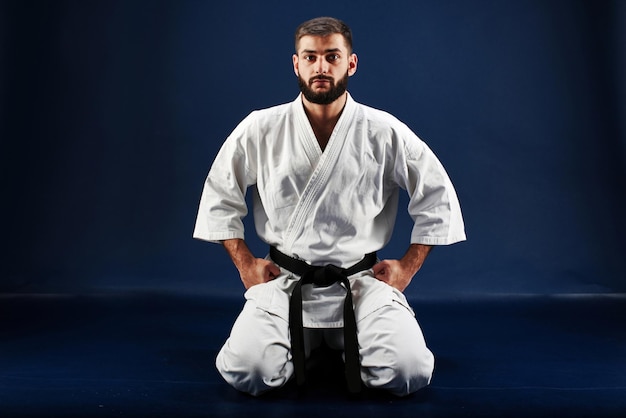 Karate-Mann in einem Kimono sitzt auf den Knien auf dem Boden auf blauem Hintergrund