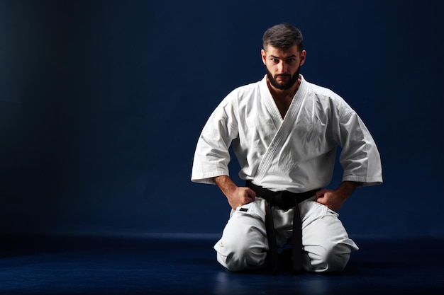 Karate-Mann in einem Kimono sitzt auf den Knien auf dem Boden auf blauem Hintergrund