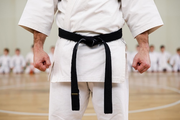 Karatemeister im weißen kimono und mit schwarzem gürtel steht vor der formation seiner schüler. kampfsportschule im training in der turnhalle.