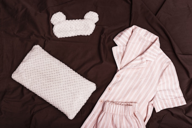 Karierter warmer Pyjama für Damen, weiches Kissen und Augenmaske zum Schlafen auf dunklem Laken auf dem Bett.