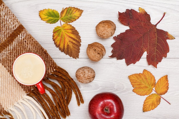 Kariertes Plaid, trockene gelbe und braune Blätter, Tasse Kaffee, Apfel und Walnüsse auf Holzhintergrund. Ein Herbststillleben. Ansicht von oben.