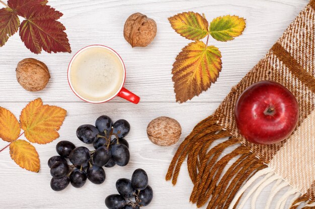 Kariertes Plaid, trockene gelbe und braune Blätter, Tasse Kaffee, Trauben und Walnüsse auf Holzhintergrund. Eine Herbstkomposition. Ansicht von oben.