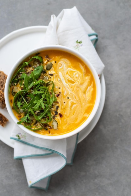 Karottencremesuppe in einer weißen Schüssel Schüssel Karottensuppe mit Rucolablättern auf Betontisch