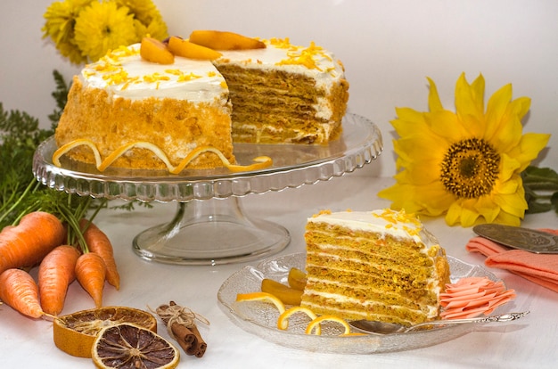 Karottenkuchentag. Mehrschichtiger Karottenkuchen auf einer weißen Oberfläche, verziert mit Orangenschale mit gelben Blüten und Karotten. Seitenansicht. Hausgemachte Kuchen