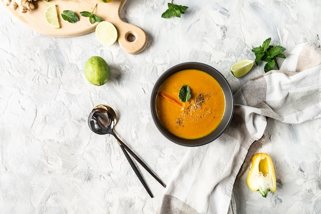 Foto karottensuppe hautnah mit frischer karotte gebackener paprika und käse-limettensaft und ingwerlöffel auf hellem hintergrund draufsicht