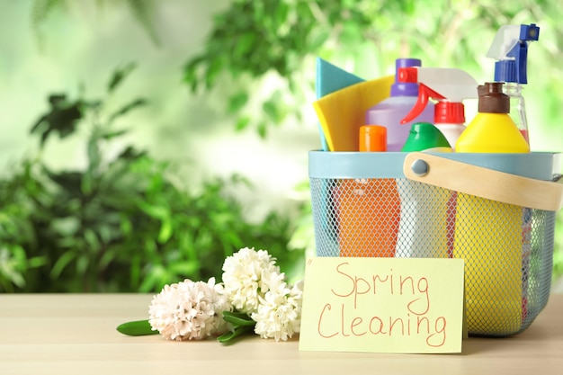 Karte mit Worten FRÜHJAHRSREINIGUNG Blumen und Reinigungsmittel auf Holztisch