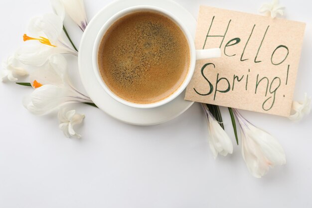 Foto karte mit worten hello frühling tasse kaffee und frische blumen auf weißem hintergrund flach gelegt