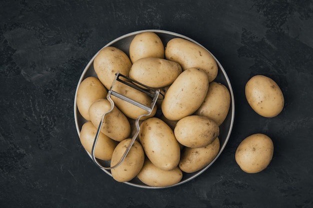 Kartoffel Frische rohe Bio-Kartoffeln in Schüssel mit Schäler auf dunklem Steinhintergrund