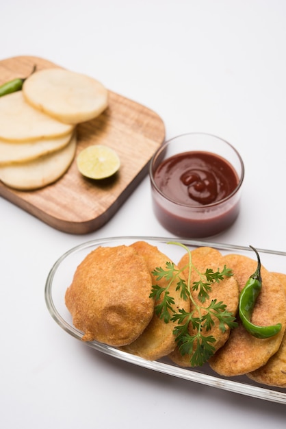 Kartoffel oder Aloo Pakora oder Pakode oder Aloo Bhajji serviert mit Tomatenketchup, grün gebratenem, kühlem und heißem Tee, beliebter indischer All-Time-Snack, serviert über frischem Kokosblatt, selektiver Fokus