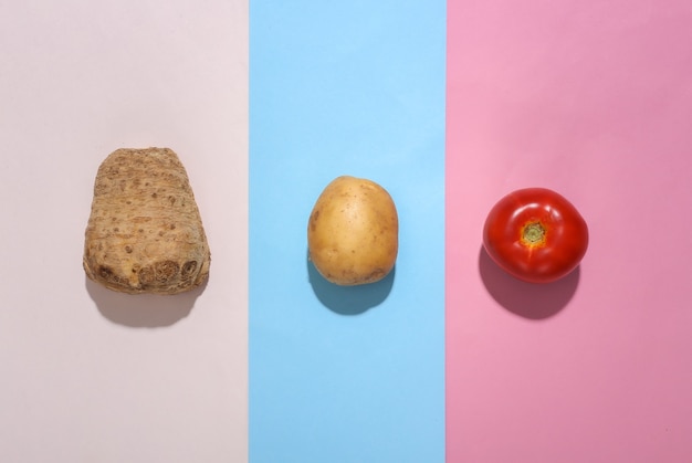 Kartoffel und Tomate, Selleriewurzel auf farbigem Pastellhintergrund. Minimalismus Essen flach. Ansicht von oben
