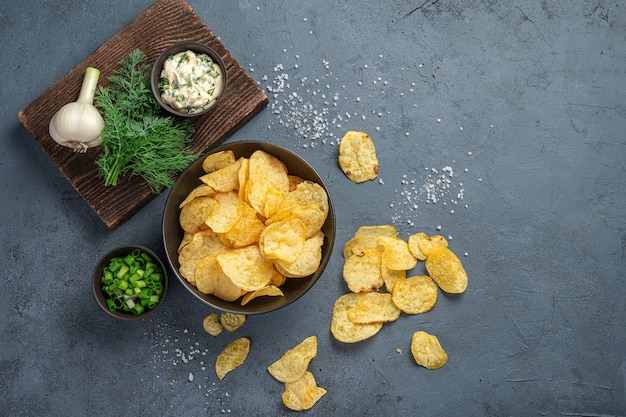 Kartoffelchips auf dunkelgrauem Hintergrund mit Zutaten. Ansicht von oben, Kopienraum.