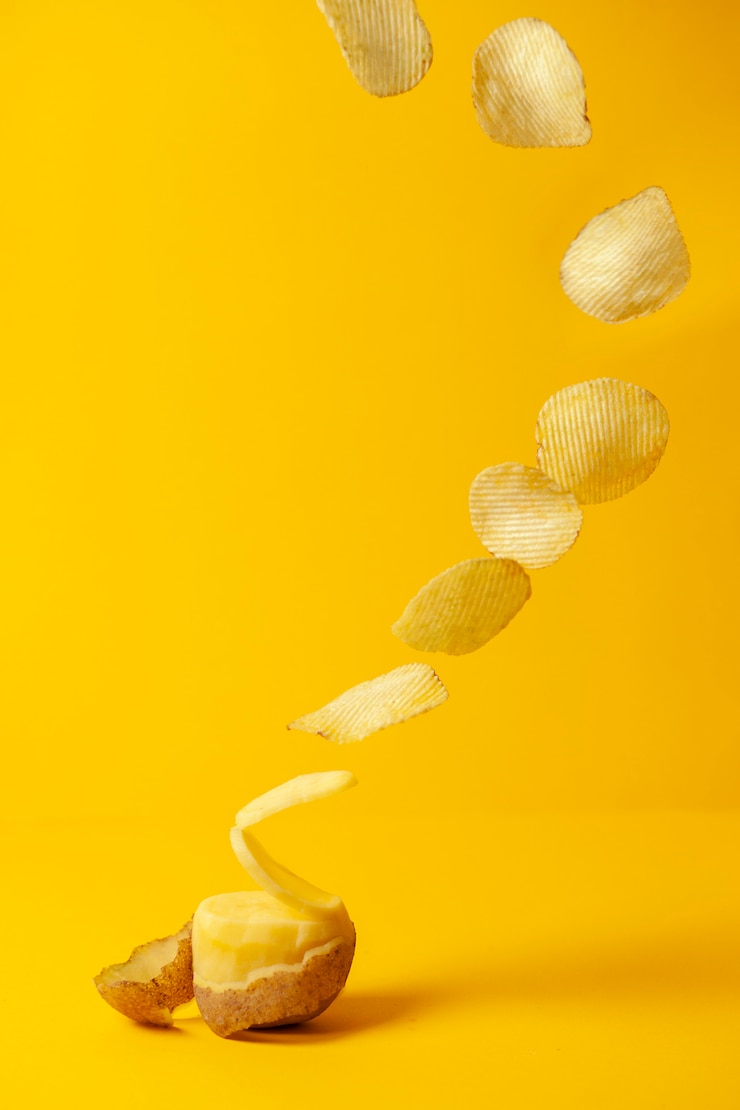 Kartoffelchips fliegen auf gelbem Grund, der Prozess der Herstellung von Chips, Fast-Food-Levitation