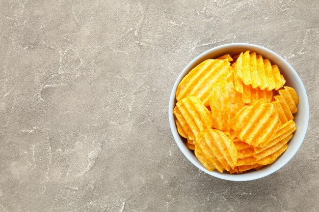 Kartoffelchips in einer Schüssel auf grauer Betonwand mit Kopienraum