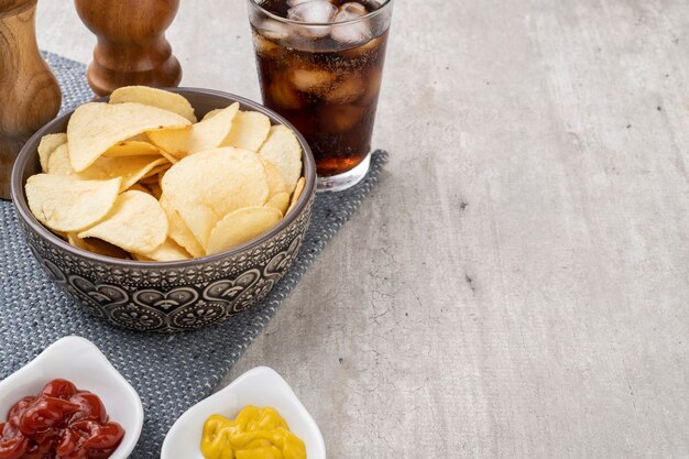 Kartoffelchips in einer Schüssel, Pfeffer, Salz, Senf, Ketchup und ein Glas Soda.