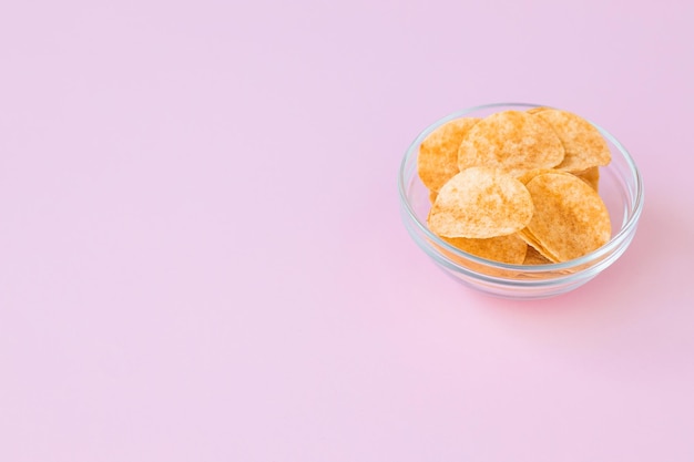 Kartoffelchips in Glasschale auf rosa Hintergrund Fast Food