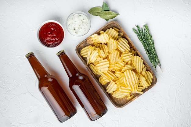 Kartoffelchips-Set mit Dip-Saucen, Tomatendip-Sauerrahm und einer Flasche Bier auf weißem Stein