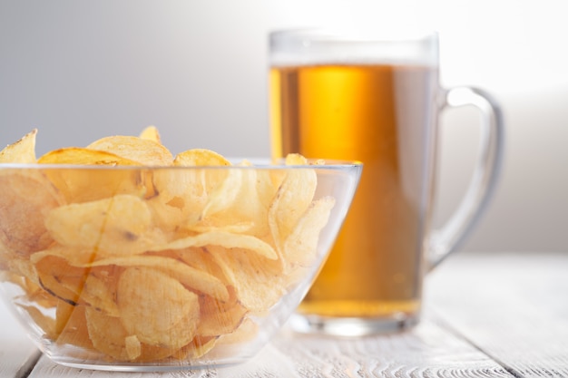 Kartoffelchips und Glas Bier auf einem Holztisch.