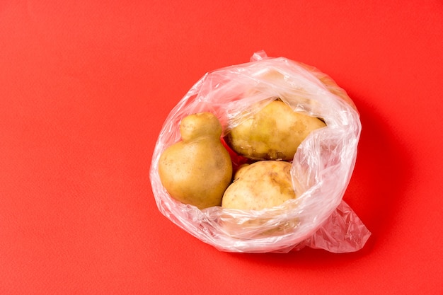 Kartoffeln in der Plastiktasche auf rotem Hintergrund. Verwenden Sie keine Aufbewahrungsbeutel für künstliche Lebensmittel mehr.
