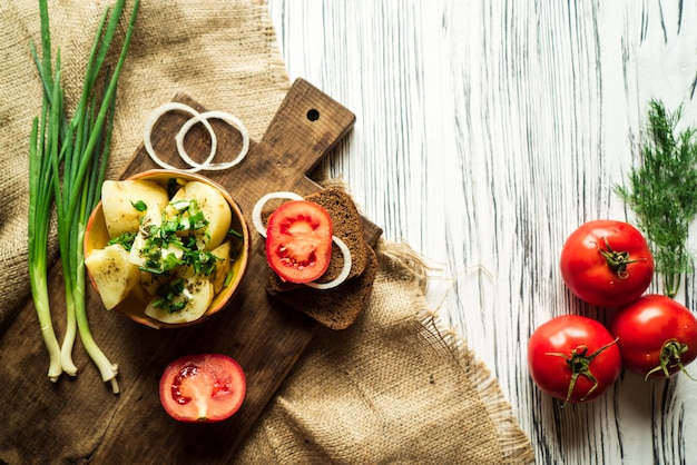 Kartoffeln, Roggenbrot, Zwiebeln, Tomaten und Grüns auf einer weißen Tabelle