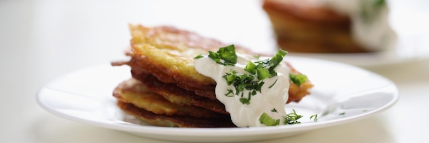 Kartoffelpfannkuchen mit Sauerrahm und Kräutern auf weißem Teller, der vegetarisches Essenskonzept kocht
