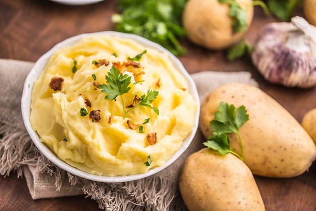 Kartoffelpüree in Schüssel dekoriert mit Petersilienkräutern und gerösteten Speckstücken.