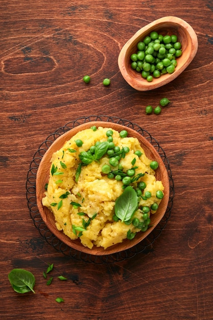 Kartoffelpüree mit Butter, Erbsen, Zwiebeln, Basilikum auf rustikalem Holzhintergrund. Ansicht von oben mit Nahaufnahme.