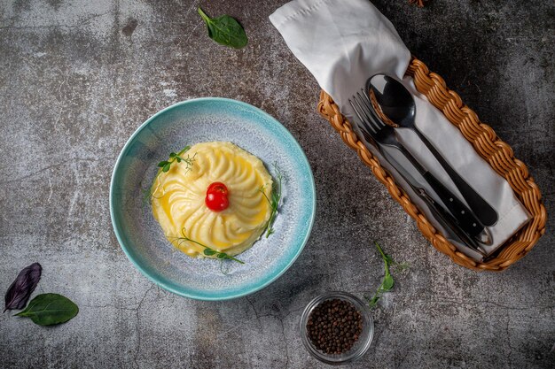 Kartoffelpüree mit frischen Tomaten auf einem blauen Teller gegen einen grauen Steintisch. Ein traditionelles, klassisches Landgericht