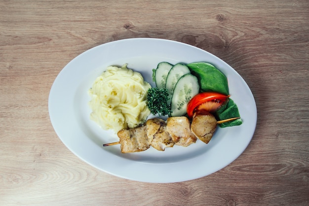 Kartoffelpüree und Kebab am Holzspieß in einem weißen Teller