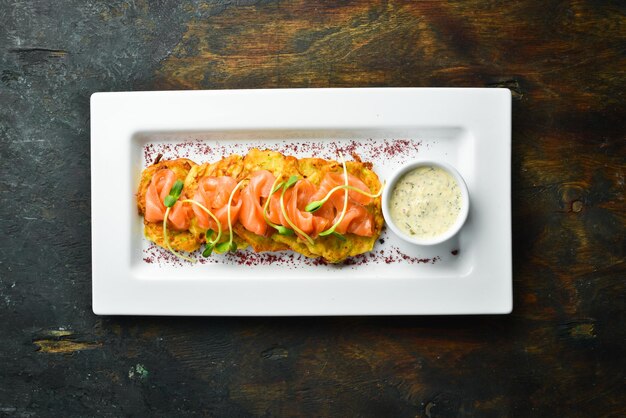 Kartoffelpuffer mit Lachs und Sauce auf einem weißen Teller. Ansicht von oben.