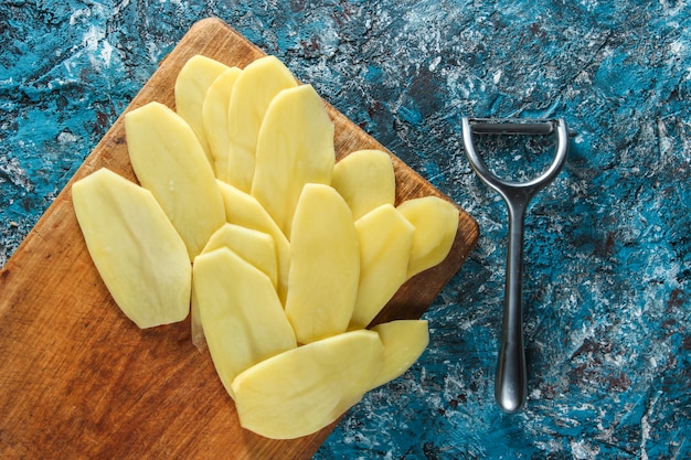 Kartoffelscheiben auf einer hölzernen Plattform auf blauem Betontisch. Draufsicht