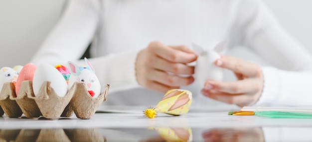 Kartonschachtel mit Osterhase-Ei-Handwerk und kaukasisches Teenager-Mädchen in weißem Turtleneck hinter dem Nähwerk-Prozess im verschwommenen