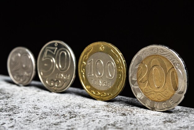 Kasachische Münzen im Wert von 20 50 100 und 200 Tenge stehen auf einem Tisch auf schwarzem Hintergrund