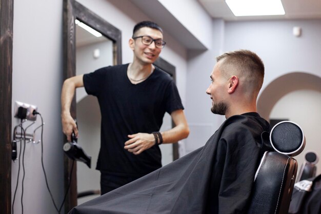 Kasachischer junger Friseur arbeitet in einem Friseur Typ sitzt in einem Friseursalon und macht einen kurzen Haarschnitt