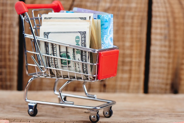 Kasachischer Tenge und amerikanische Dollar in einem Spielzeug-Einkaufswagen auf einer hölzernen Hintergrundnahaufnahme. Konzept für Wirtschaft und Finanzen. Isoliert.