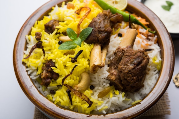 Kashmiri Mutton Gosht oder Lamm Biryani zubereitet in Basmati-Reis serviert mit Joghurt-Dip über stimmungsvollem Hintergrund, selektiver Fokus