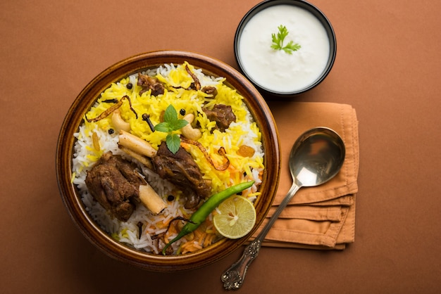 Kashmiri Mutton Gosht oder Lamm Biryani zubereitet in Basmati-Reis serviert mit Joghurt-Dip über stimmungsvollem Hintergrund, selektiver Fokus