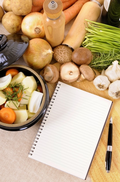 Kasserollentopf mit organischem Gemüse und Kräutern auf Küche worktop mit leerem Kochbuch oder Rezeptbuch