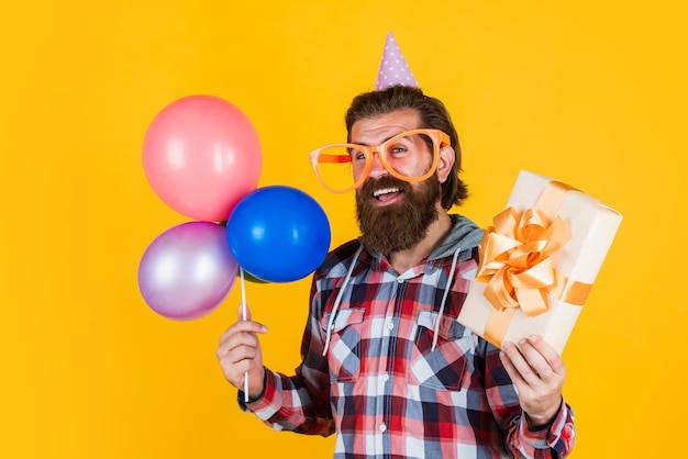 Kauf und Verkauf von Party-Elementen und Urlaubsobjekten Mehrfarbiger Spaß beste Party für den Ruhestand Fröhlicher Mann mit Bart hält anwesenden Hipster lächelnd mit Ballon Feiert eine fröhliche Party