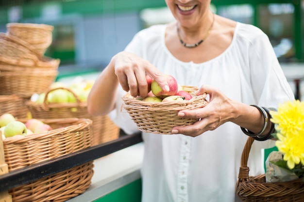 Kaufende Äpfel der älteren Frau im Spannkorb auf Markt