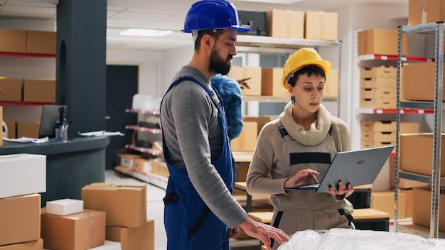 Foto kaukasier analysieren warenlisten auf einem tablet und arbeiten im lager mit einzelhandelswaren und kartons. vorgesetzter gibt dem arbeiter aufgaben und organisiert produkte in regalen und gestellen.