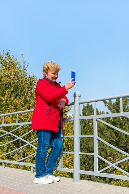 Kaukasische ältere Frau in der roten Jacke unter Verwendung des Smartphones im Park