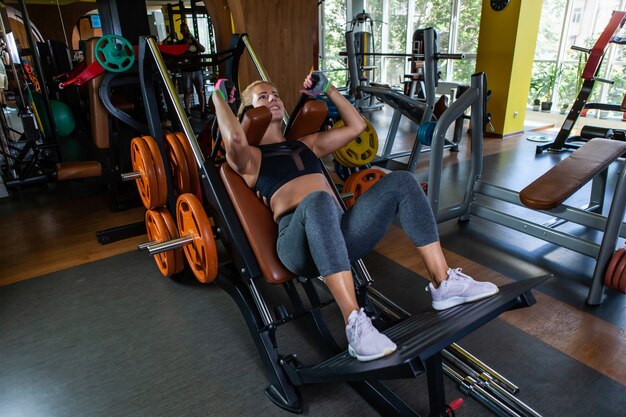 Kaukasische attraktive Frau, die Kniebeugen im Trainingsgerät im Fitnessstudio übt