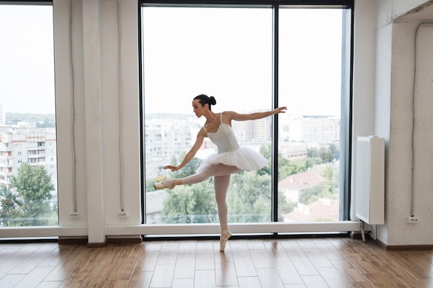 Kaukasische Ballerina posiert in einem hellen Klassenstudio mit Panoramafenstern