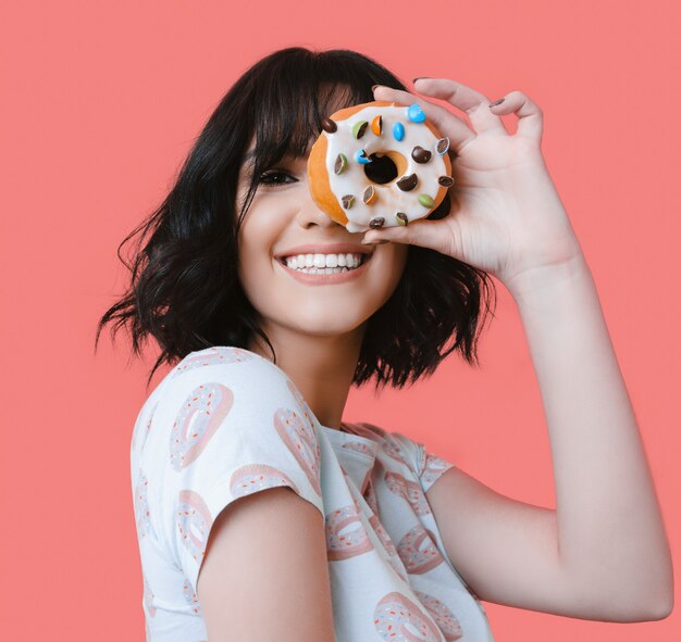 Kaukasische brünette frau, die einen leckeren donut lächelnd hält