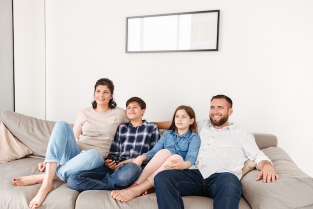 Kaukasische familie mit zwei kindern, die zu hause im wohnzimmer ruhen und zusammen fernsehen, während sie auf dem sofa sitzen