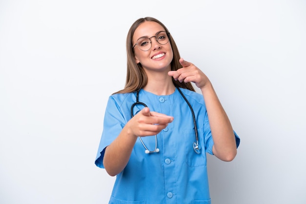 Kaukasische Frau der jungen Krankenschwester, die auf weißem Hintergrund lokalisiert wird, zeigt Finger auf Sie beim Lächeln